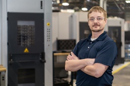 Man in protective goggles stands with his arms crossed on a factory floor