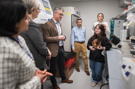 A female student talks to a group of several men and women in a lab setting